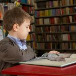 boy sitting near red table reading book