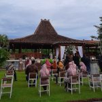 people sitting on chairs near brown wooden house under white clouds during daytime