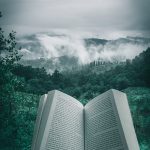 person holding open book viewing mountain view