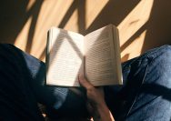 person holding book sitting on brown surface